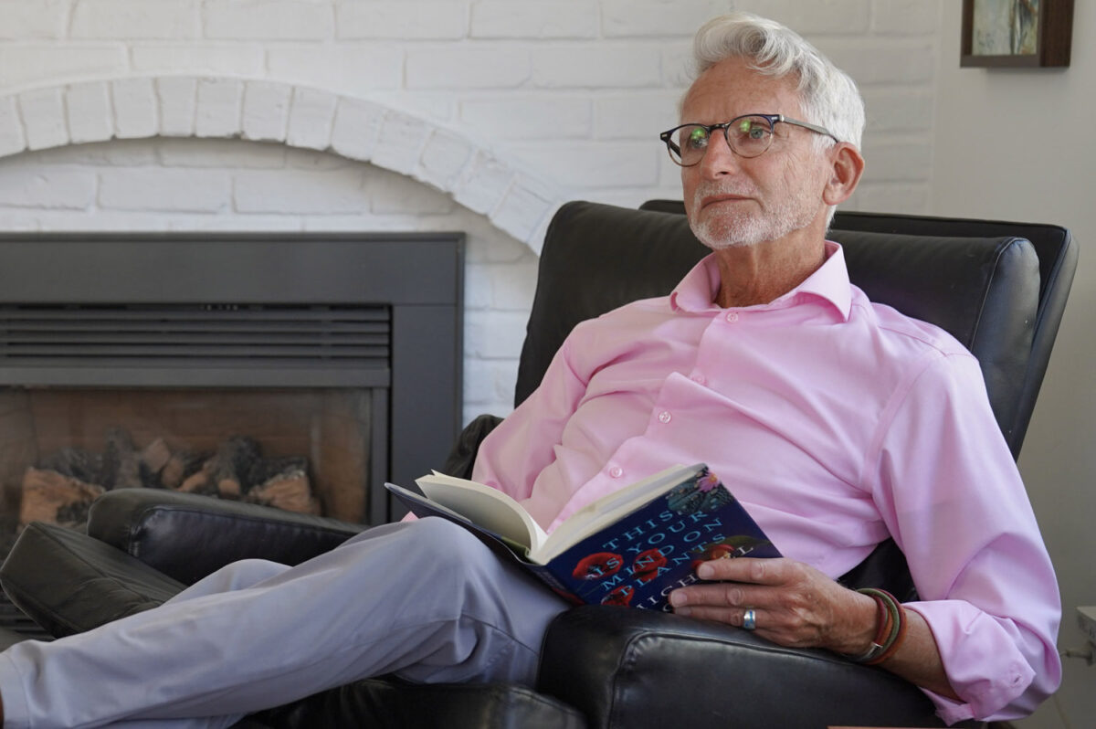 Timm sitting in a chair by a fireplace with a book open on his lap